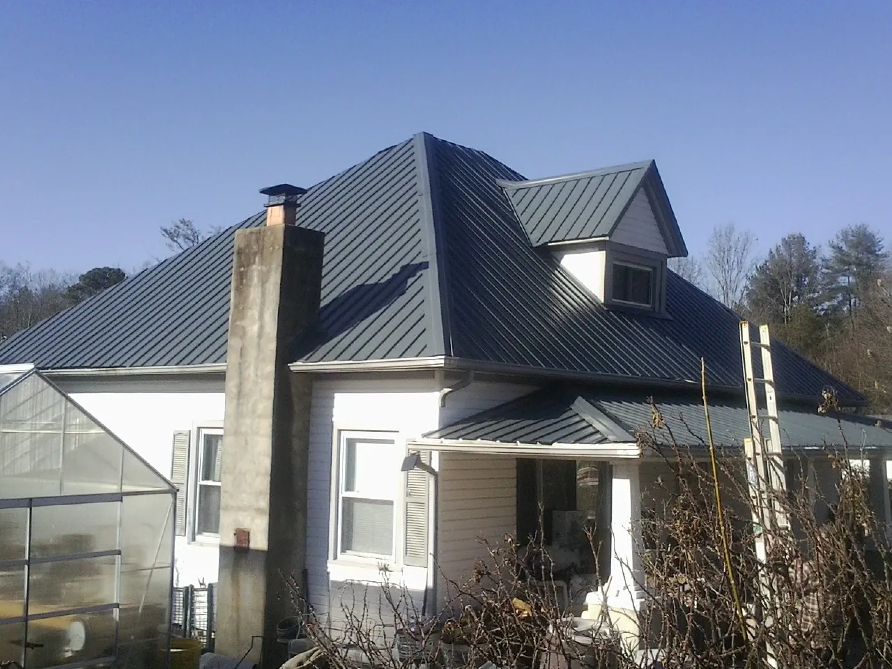 Dark blue standing seam metal roof on a white farmhouse with dormer — Slate & Tile Roof Repair by Roofing Brothers in Varna