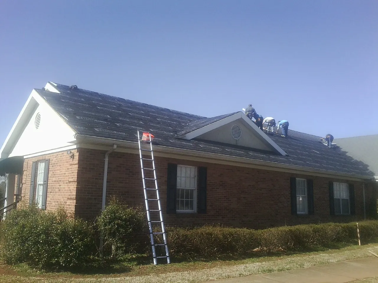 Crew tearing shingles off a brick ranch roof with a ladder set — Emergency Roof Repair work by our crew in Varna