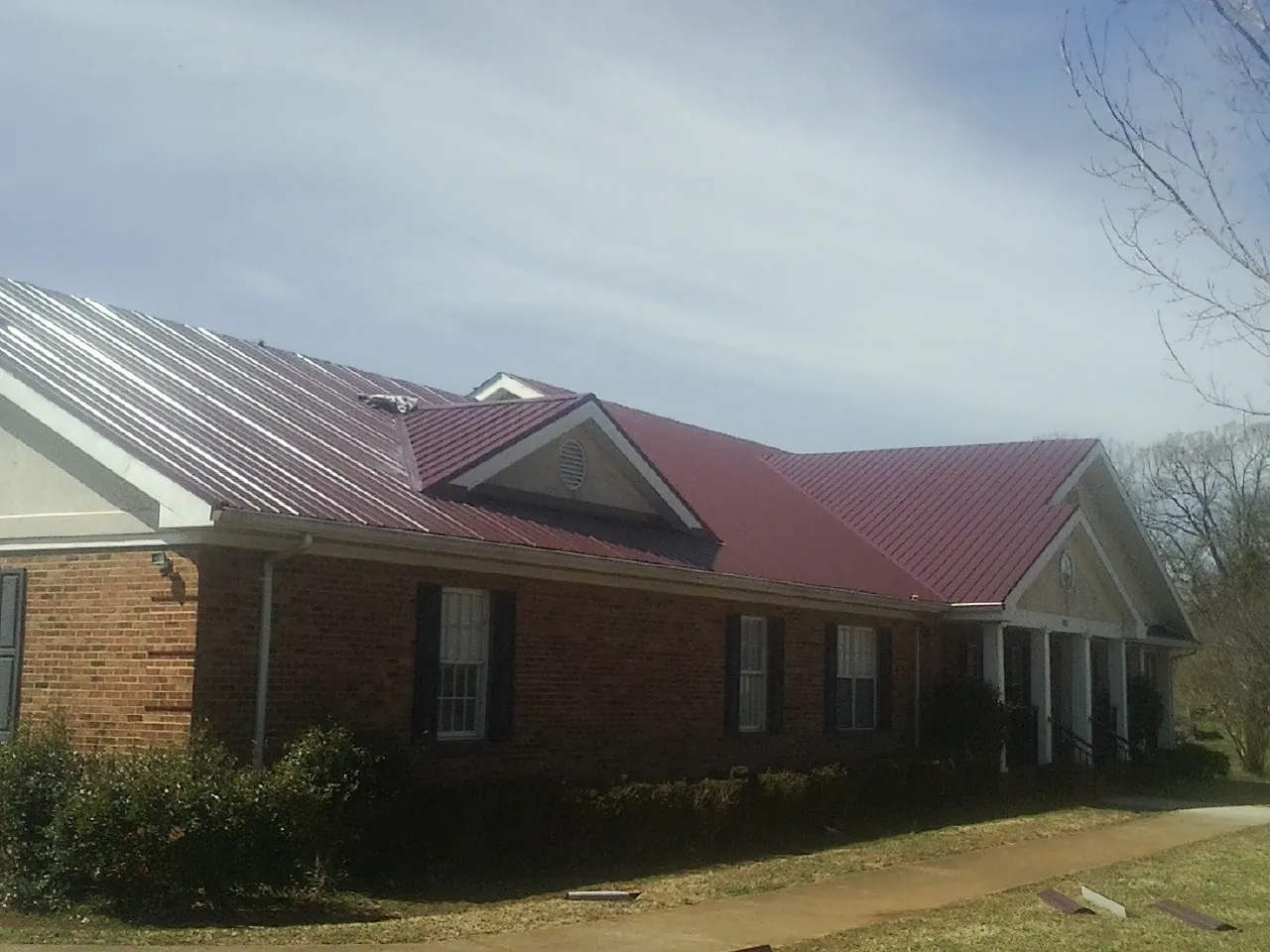 Red metal roof with gabled entries on a long brick building, from a Hail Damage Roof Repair job in Varna