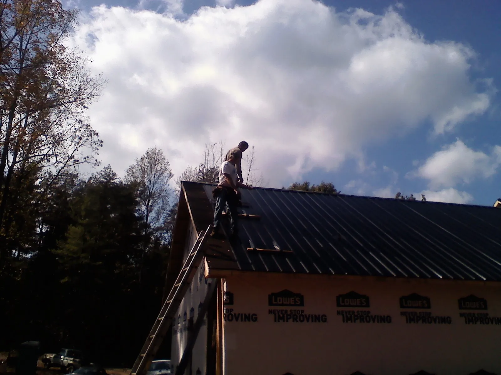 Roofer fastening dark metal panels high against a cloudy sky, from a Roof Inspection job in Varna
