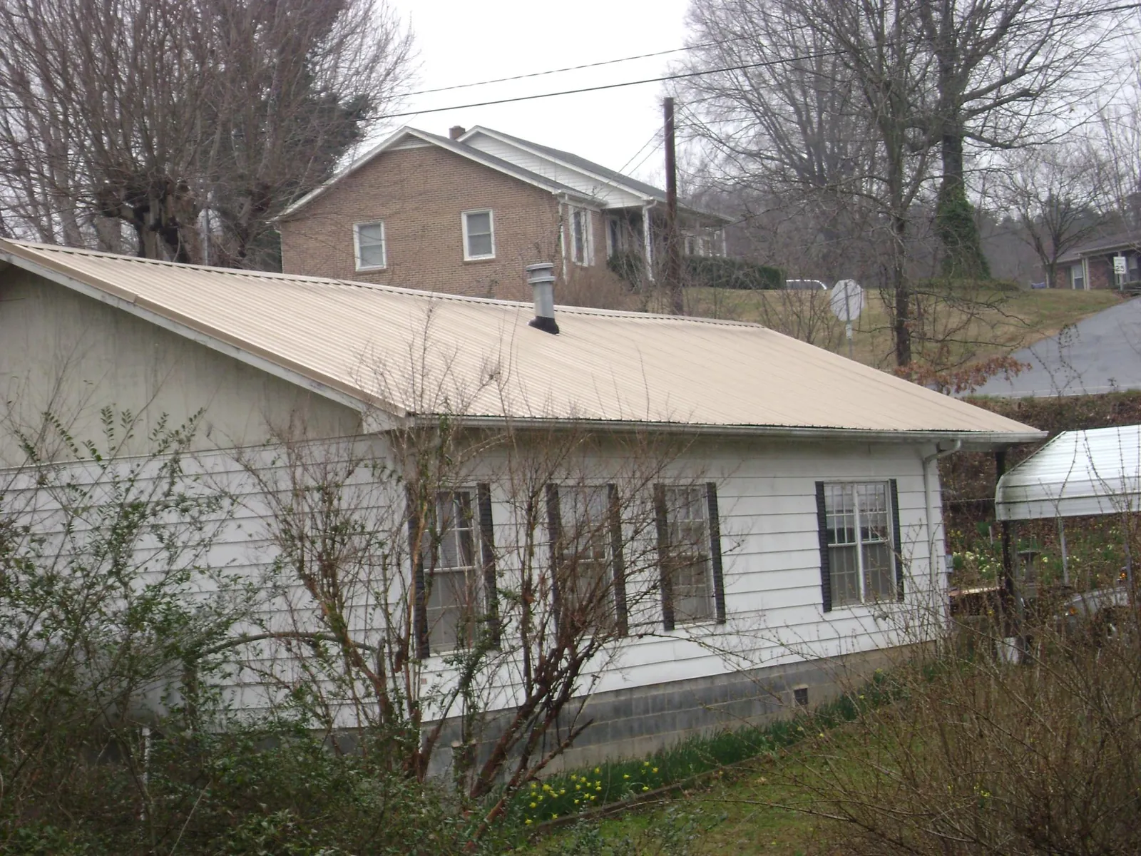 Tan metal roof on a white sided house set into a hillside — Commercial Roofing by Roofing Brothers in Varna